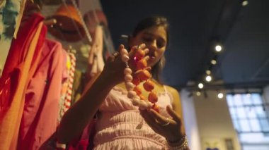 Genç bir kız şık bir butikte alışveriş yaparken sergilenen canlı ve renkli mücevherlere heyecanla hayran.