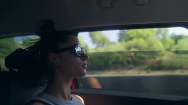 Dışarıda güzel manzaralı bir yolculuğun tadını çıkarırken, genç bir kadın dikkatlice araba camından dışarı bakıyor.