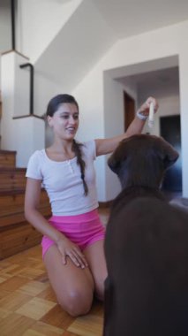 Genç bir kız enerjik köpeğiyle mutlu bir şekilde oynuyor, kapalı bir ortamda neşeli ve eğlenceli bir bağ sergiliyor.