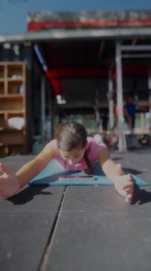 Genç bir kız açık havada renkli bir minder üzerinde yoga yapıyor, güneşli bir ortamda odak ve rahatlama gösteriyor.