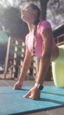 Genç bir kız dışarıda yoga yapıyor. Açık havada poz veriyor. Parlak güneş ışığı altında esneklik ve güç gösteriyor..