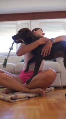 Bir kadın içeride sevgili köpeğiyle neşe içinde etkileşime geçiyor, eğlenceli bağlarını ve bağlarını sergiliyor.