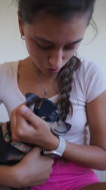 Genç bir kadın, sıcak ve rahat bir ortamda sevgi dolu bağlarını gösteren küçük bir köpeği nazikçe tutuyor.