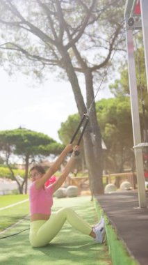 Bir kadın direniş bantlarıyla egzersiz yapıyor, güzel bir açık hava spor salonundan faydalanıyor.