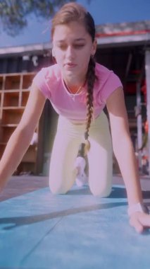 Son derece odaklanmış ve kararlı genç bir kız yoga minderinin üzerinde canlı bir açık hava ortamında çeşitli egzersizler yapıyor.