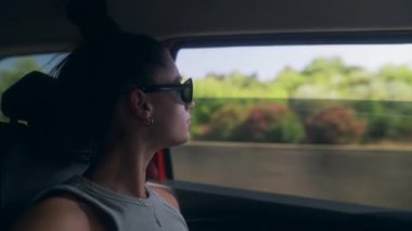 Bir kadın düşünceli bir şekilde araba camından dışarı bakar, seyahat ederken güzel manzaranın tadını çıkarır.