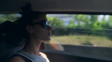 Şık güneş gözlüklü bir kadın rahatlatıcı bir araba yolculuğu sırasında güzel ve manzaralı bir kır manzarasının tadını çıkarıyor.