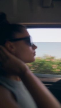 Güneş gözlüğü takan şık bir kadın okyanus manzarası boyunca sakin bir şekilde araba sürmekten zevk alır.