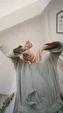 Huzurlu bir iç mekan sahnesi, rahat bir bornoz giymiş, büyüleyici ve sanatsal el hareketleri yapan birini gözler önüne seriyor.