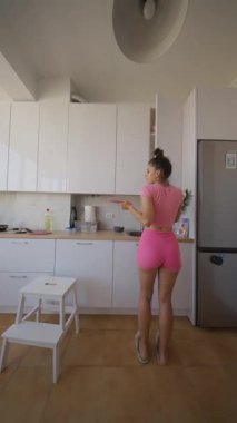 Modern mutfağında lezzetli yemekler hazırlayan şık genç bir kadın parlak bir kıyafet giyiyor.