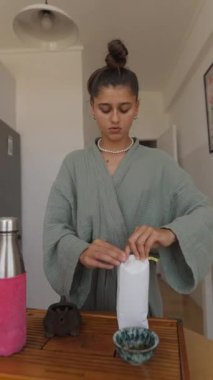 Canlı yeşil bir bornoz giymiş bir kadın düzenli olarak çay hazırlar, mekanını sıcaklık ve sükunetle doldurur.