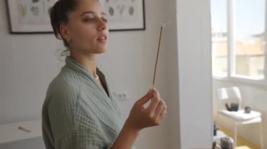 Bir kadın, sakin ve huzurlu bir ortamda elinde bir tütsü çubuğu tutarken derin bir şekilde meditasyon durumuna sarılır.