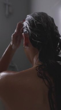 Duşta şampuan süren, saç bakımını canlandıran ve canlandıran bir kadın.