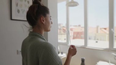 Bir kadın parlak, güneşli bir odada yaratıcı işleriyle çok ilgilidir. Düşünceli bir şekilde bir sopa tutar.