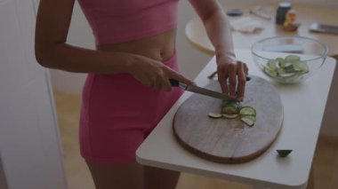 Canlı pembeler içindeki bir kadın taze salatalıkları ustalıkla dilimliyor ve sağlıklı pişirme becerilerini hassasiyetle sergiliyor.