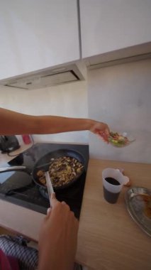 Yetenekli bir birey, canlı ve renkli bir yemek hazırlıyor ve sıcak tavaya taze sebzeler ekliyor.