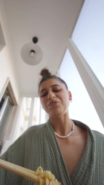 Zarif, şık ve güneşli bir ortamda yemek çubuklarıyla lezzetli eriştelerin tadını çıkaran bir kadın.