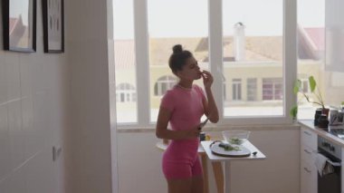 Parlak bir mutfakta sağlıklı bir yemeğin tadını çıkaran bir kadın, hayat dolu ve sağlıklı bir yaşam tarzını somutlaştırıyor.