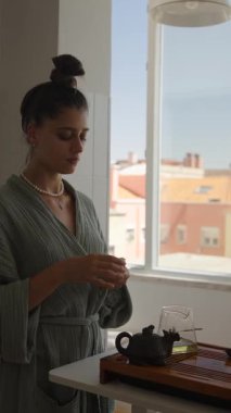 Sıcak, güneşli bir mutfakta çay içen sakin bir kadın sahnesi, sükunet ve farkındalığın vücut bulmuş hali..