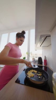 Genç bir kadın, doğal ışıkla dolu parlak ve şık bir mutfakta zevkli bir kahvaltı hazırlar.