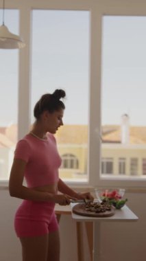 Pembe elbiseli bir kadın, güneşli bir mutfakta ustalıkla lezzetli bir yemek hazırlıyor.