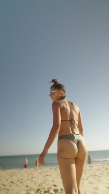 Bir kadın kumsalda geziniyor, güneşin ve yumuşak kumların tadını çıkarıyor, yaz mutluluğunun özünü yakalıyor.