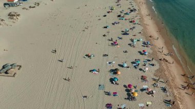 Hava görüntülerinde güneş banyosu yapan ve güneş koruması için canlı şemsiyelerle dolu yoğun bir plaj gösteriliyor.
