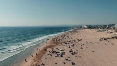 Kalabalık bir plajın çarpıcı ve manzaralı manzarası, gösterişli sörfçüler, güneşlenenler ve güzel sahil şeridi.