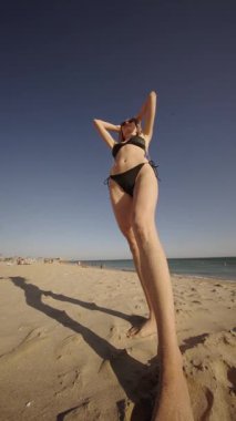 Canlı bir plaj sahnesinde neşeli bir manken güzel sahil boyunca güneşli günün tadını çıkarıyor.