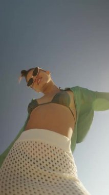 Neşeli bir kumsalcı güneşli bir günün tadını çıkarıyor, canlı yaz modasını sergiliyor ve pozitifliğini yayıyor.