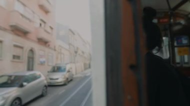 Bir kadın düşünceli bir şekilde tramvay penceresinden bakar, çarpıcı şehir manzarasını ve hareketli çevreyi seyreder.