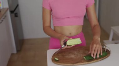 Modern bir mutfak ortamında, genç bir kadın ustalıkla dilimlenmiş salatalıkları ustalıkla hazırlar.