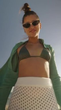 Neşeli genç bir kadın son moda bikini ve güneş gözlükleriyle plaj gününün tadını çıkarıyor.