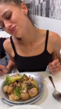 Sıcak bir restoranda, genç bir kadın lezzetli patates ve taze sebzelerle lezzetli bir yemeğin tadını çıkarıyor.