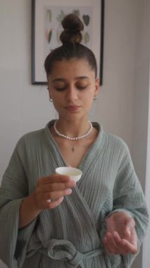 Genç bir kadın dinlenmek ve güzelleşmek için tasarlanmış sakin, parlak bir alanda rahatlatıcı bir cilt bakımı yapar.