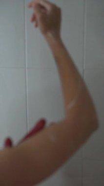 Bir birey duşa sabun sürüyor, ferahlatıcı ve arındırıcı bir rutin sergiliyor.