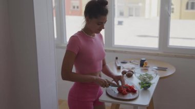 Parlak ve neşeli bir mutfakta, bir kadın özenle taze sebzeler hazırlar, sağlık ve canlı renkleri vurgular.