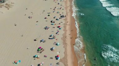Şemsiyeli, kumlu ve okyanus dalgalı canlı plaj sahnesi, rahatlama ve yaz aktiviteleri için mükemmel..
