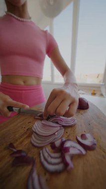 Günümüz güneşli mutfağında, bir kadın etkileyici mutfak becerilerini göstermek için canlı kırmızı soğanları ustalıkla dilimliyor.