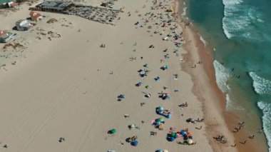 Canlı bir plajın göz kamaştırıcı bir görüntüsü. Renkli şemsiyeler ve güneşin tadını çıkaran kumsala gidenlerle dolu.