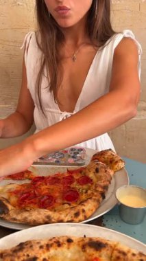 Canlı bir lokantada büyük bir biberli pizzanın tadını çıkaran bir kadın yiyeceği paylaşmanın esansını yakalıyor.