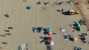 Göz kamaştırıcı bir hava manzarası canlı şemsiyeler, güneşli banyolar ve rahat havlularla dolu canlı bir plaj sahnesi yakalar.