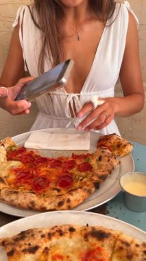 Lezzetli bir pizzanın tadını çıkaran bir kadın telefonuyla şık bir ortamda keyifli bir anı yakalıyor.
