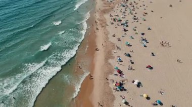 Güneş banyosu ve renkli şemsiyelerle dolu canlı bir plajın nefes kesici hava manzarasının tadını çıkarın..