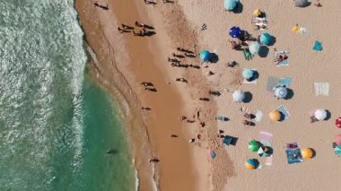 Renkli şemsiyeler, güneş banyosu ve saf, kristal berrak suyla dolu hareketli bir plaj manzarası.