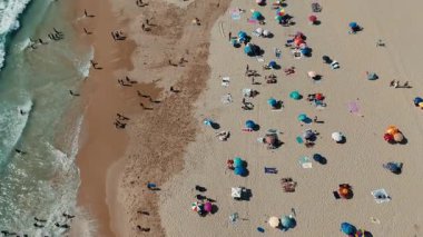 Canlı bir plaj sahnesi. Renkli şemsiyeler ve güneşli bir günün tadını çıkaran sayısız güneşli banyo.