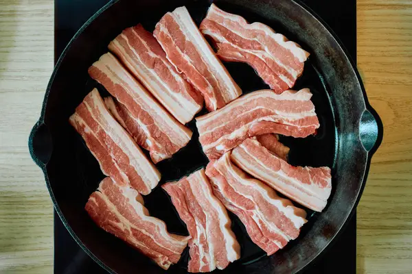 Pişmemiş domuz eti dilimleri dökme demir tavada dizilmiş. Barbekü, kızartma ya da geleneksel tarifler için mükemmel. Taze etin pişirilmeye hazır olduğu yakın çekim görüntüsü.