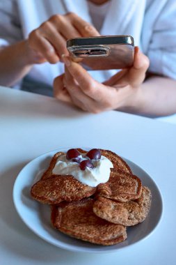 Kahvaltı ederken elinde akıllı telefon tutan bir kişi, modern hayatta sürekli telefon kullanımı ve teknoloji bağımlılığının görsel bir metaforudur..