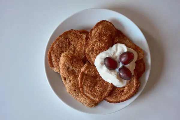 Badem unundan yapılmış ev yapımı keto krepleri kremalı Yunan yoğurdu ve taze kırmızı üzümle servis ediliyor. Dengeli beslenme ve şekersiz yaşam tarzı için lezzetli ve sağlıklı düşük karbonhidratlı kahvaltı.