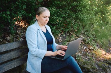 Park yerinde dizüstü bilgisayarla çalışan bir kadın. Serbest ya da çevrimiçi iş kavramı. Açık hava çalışma alanı, üretkenlik, doğa.